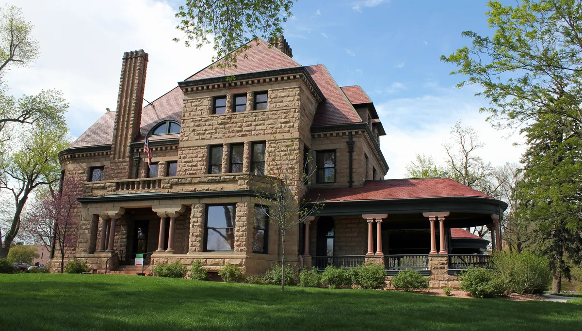 Rosemount mansion on a sunny spring day, its warm stone walls and wraparound veranda framed by green lawn